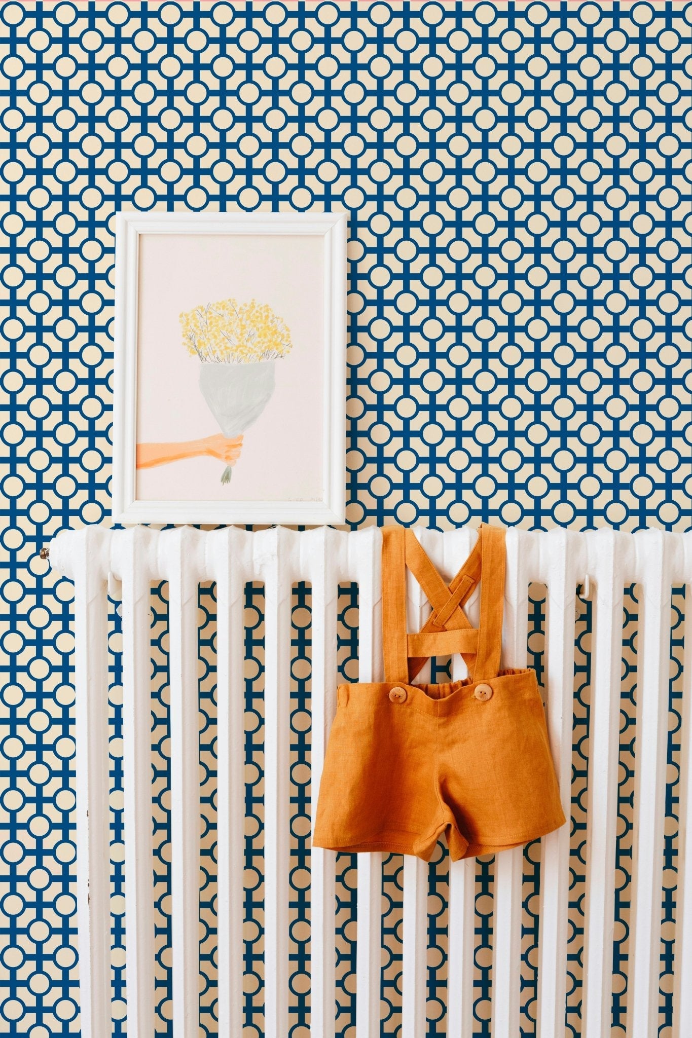 retro trellis wallpaper in blue in a nursery with a framed art print and tiny overalls for a baby