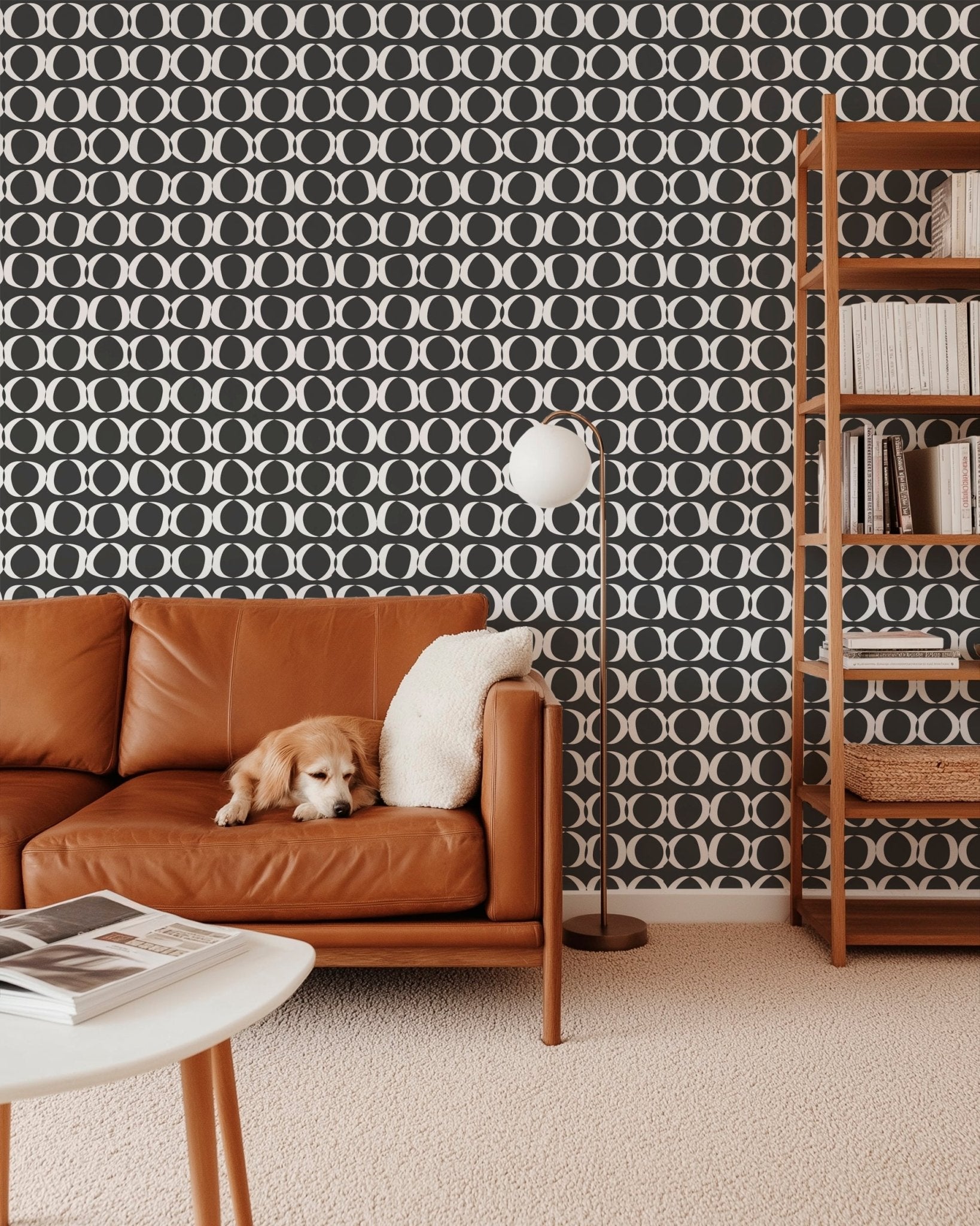 Gray and white abstract circles wallpaper in a living room with a brown leather couch and wooden book shelf
