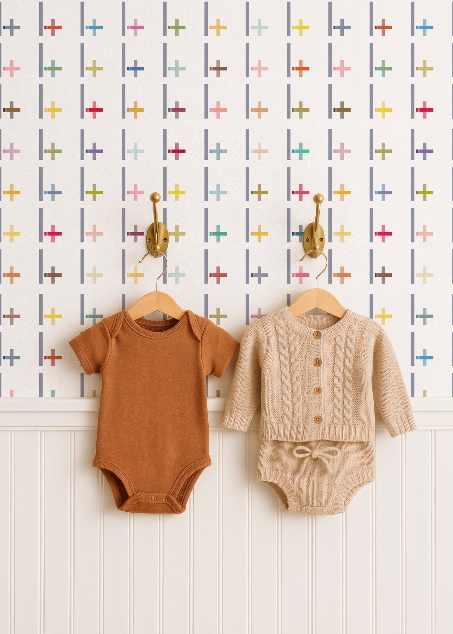 Two baby outfits on hangers against a patterned wall.