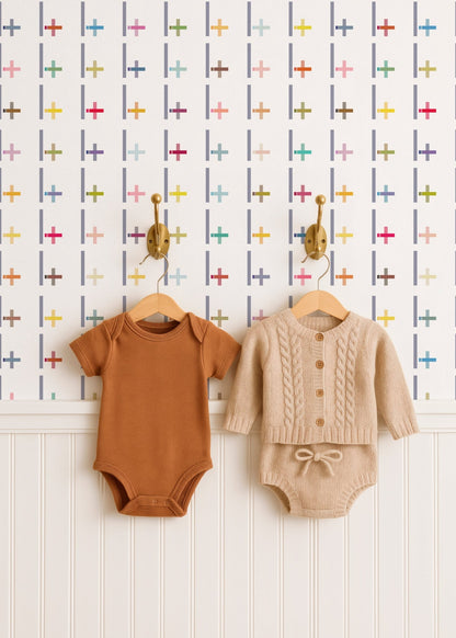 Two baby outfits on hangers against a patterned wall.