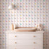 White dresser with a wicker tray, bottle, and plush toy against a multicolored geometric patterned wall.